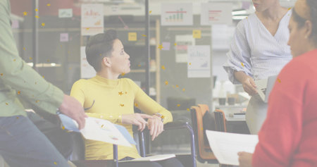 Woman in wheelchair in yellow top leading discussion with colleagues in office, with laptop charts. Collaboration, teamwork, inclusivity, innovation, corporate, communication, brainstormingの写真素材
