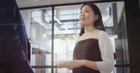 Chatting businesswoman wearing dress near glass wall in office, with metal framing and exit sign. Professional, corporate, modern, minimalist, workspace, collaboration, brightnessの写真素材