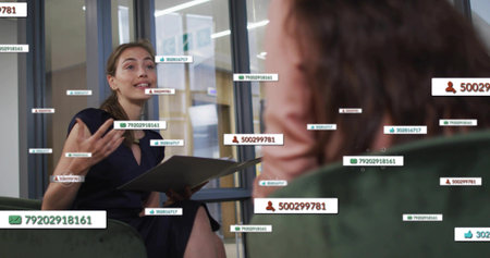 Gesturing fair-skinned woman holding folder on green chair in meeting room, displaying data labels. Professional, teamwork, collaboration, corporate, modern, data, communicationの写真素材