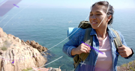 Adjusting straps hiker in denim shirt on rocky coast, with green pack, blue mat, copy space....