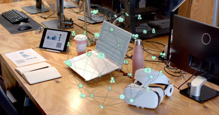 Displaying silver laptop with network icons overlay on office desk, with tablet and coffee cup....