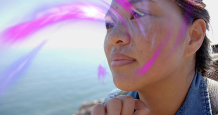 Gazing Asian woman wearing denim jacket carrying backpack on rocky shore, purple light, copy space....