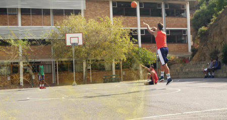 Shooting male athlete releasing basketball toward hoop on outdoor court by large tree, copy space....