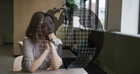 Resting chin on hand, Asian woman gazing at wireframe globe overlay in coworking lounge, copy space. Businesswoman, minimalist, futuristic, collaboration, innovation, urban, workspaceの写真素材