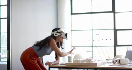 Leaning mid adult Indian designer scanning AR interface with headset in studio, with scale models....
