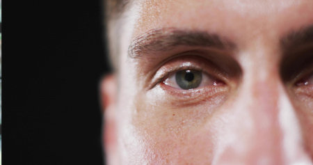 Focusing close up on mid adult man's green eye on dark studio backdrop, highlighting skin texture. Portrait, beauty, detail, contrast, intensity, minimalism, wellnessの写真素材