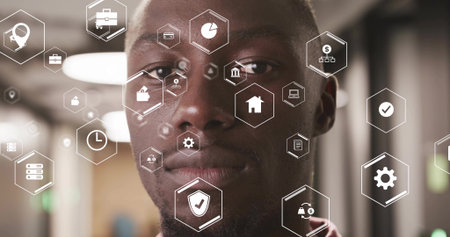 Standing black male professional wearing collared shirt in office hall with hexagon interface icons. Technology, innovation, corporate, digital, futuristic, executive, networkingの写真素材
