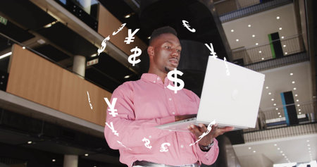 Business professional holding laptop and analyzing data in atrium, with floating currency symbols....