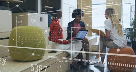 Collaborating three coworker women using laptop, tablet and holding yellow folder in office lounge. Coworking, teamwork, innovation, modern, productivity, casual, collaborationの写真素材