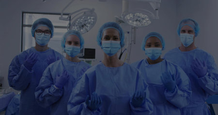 Standing five medical staff adjusting gloves in operating room, wearing blue gowns and hair caps....