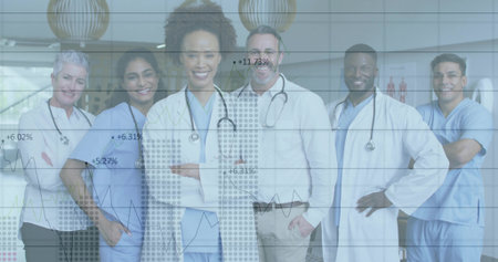 Posing medical team wearing blue scrubs and stethoscopes in clinic lobby, with overlaid line graphs. Healthcare, teamwork, professionalism, modern, facility, analytics, hospitalの写真素材