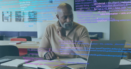 Touching chin mature man while scanning code on laptop at office, with notebooks, papers. Technology, workspace, professional, concentration, innovation, contemporary, collaborationの写真素材