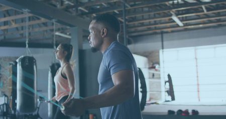 Skipping man wearing navy T-shirt and shorts holding jump rope in boxing gym, with punching bags. Fitness, training, sport, vitality, inspiration, athletic, motionの写真素材