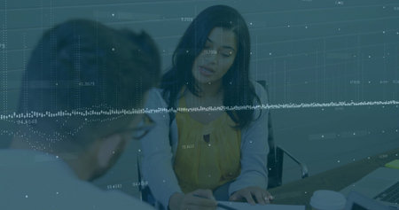 Woman in yellow blouse examining paperwork on desk in office meeting area, with laptop, coffee cups. Collaboration, professionalism, workspace, business meeting, teamwork, modern, corporateの写真素材