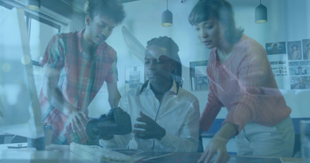 Holding VR headset, seated man wearing white shirt in office with monitor and coworkers leaning. Collaboration, technology, innovation, modernity, teamwork, creative, workspaceの写真素材