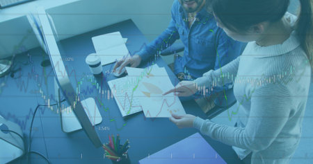 Professionals in office attire reviewing charts and graphs at desk near window, with data overlays. Corporate, teamwork, analytics, data, technology, workspace, collaborationの写真素材