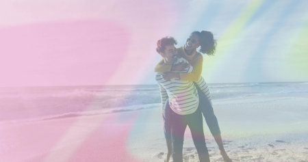 Laughing couple sharing piggyback ride on sandy shoreline, with mustard sweater and sunglasses. Romance, leisure, carefree, outdoor, serenity, adventure, joyの写真素材