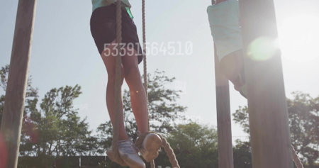 Climbing boy wearing shirt and shorts gripping thick ropes on wooden posts at outdoor playground. Adventure, childhood, activeplay, nature, resilience, teamwork, vibrantの写真素材