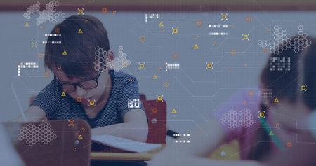 Writing boy in glasses concentrating on notebook at wooden desk in classroom, with digital overlay....