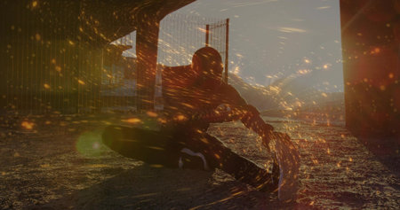 Dancing man in hoodie weaving spark-like lights on gravel under overpass pillars, fence at dusk. Urban, silhouette, motion, energy, nightlife, gritty, abstractの写真素材