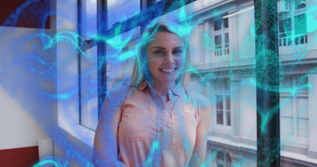 Smiling woman wearing peach top by office window near red windowsill as blue-green overlay swirling. Professional, urban, technology, modern, business, networking, connectivityの写真素材