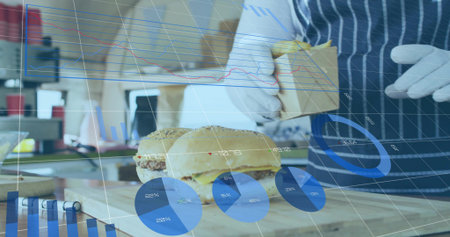 Cook wearing striped apron with gloves lifting burger into box at prep station with data overlay. Fast food, kitchen, packaging, analytics, technology, culinary, serviceの写真素材