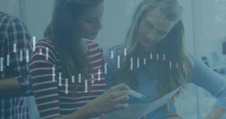 Two women reviewing printed document in office, with green-tipped marker, chairs and monitors. Collaboration, teamwork, productivity, business, professional, modern, discussionの写真素材