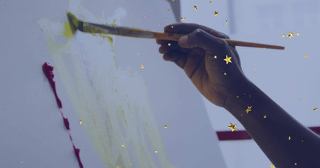 Applying yellow-green wash to canvas in art studio with paintbrush, gold star confetti, copy space. Artistry, creativity, abstract, vibrant, inspiration, craftsmanship, modernの写真素材