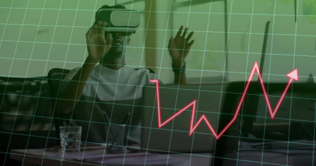 Man wearing VR headset manipulating interface in office, with laptop, grid overlay and line graph. Technology, innovation, digital, immersive, futuristic, analytics, workspaceの写真素材