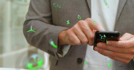Holding smartphone, senior man wearing blazer raising phone in office with floating eco icons....