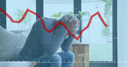 Leaning man covering face with hands on light-colored couch at home, with red line graph overlay. Stress, anxiety, financial, contemplation, home, interior, modernの写真素材