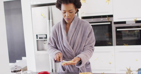 Woman wearing bathrobe spreading jam from jar on bread slice at kitchen island, with butter knife. Bedroom, comfort, wellness, home, hygiene, relaxation, lifestyleの写真素材