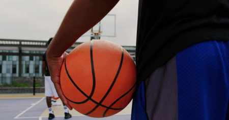 Basketball player in sportswear holding ball on outdoor court, with hoop and copy space. Athletics,...