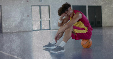 Basketball player in red yellow uniform sitting on orange basketball in gym with sweatbands, shoes....