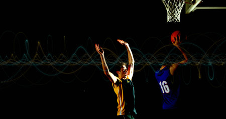Leaping player wearing blue jersey holding basketball toward hoop and net on dark court, copy space....