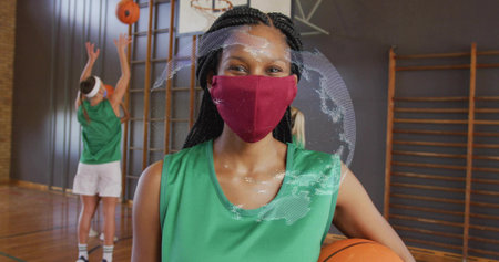 Holding female athlete wearing green jersey face mask holding basketball in gym, with climbing bars....