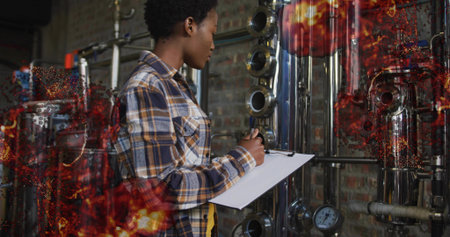 Checking gauges, technician wearing plaid shirt beside steel tanks at plant holding clipboard....