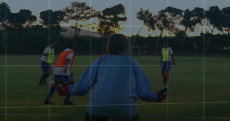 Standing female goalkeeper wearing light blue jersey in grass field at dusk, with soccer ball. Athletics, training, teamwork, sportsmanship, landscape, vibrant, activeの写真素材