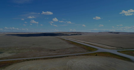 Showcasing highway intersection cutting across open farmland under blue sky, with farm buildings. Rural, landscape, transportation, aerial, agriculture, scenic, tranquilityの写真素材