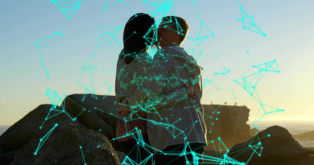 Embracing couple standing on rocky boulders overlooking ocean during sunset, with turquoise network. Romantic, connection, tranquility, serenity, landscape, abstract, cohesionの写真素材