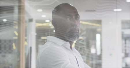 Standing man wearing white shirt and gazing in modern office, behind decorative glass partition....