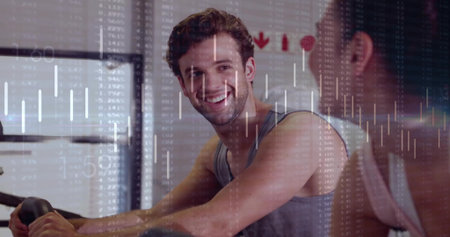 Pedaling man in sleeveless shirt glancing at partner at gym with bikes and financial chart overlay....