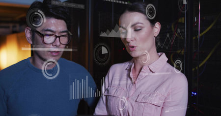 White woman and Asian man studying data visualization on glass panel in server room, with racks. Futuristic, collaborative, digital, technology, innovation, analysis, networkingの写真素材