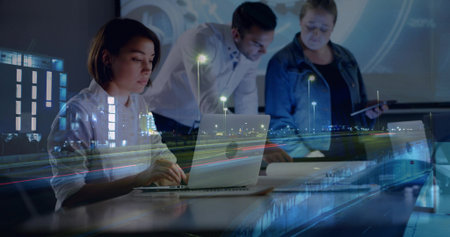 Typing female team member sitting at laptop in meeting room, with documents and projection screen. Collaboration, teamwork, innovation, modern, professional, urban, digitalの写真素材
