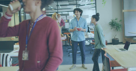 Holding red coffee mug, Hispanic man wearing blue shirt in open-plan office, with sticky notes. Collaboration, teamwork, modernity, workstation, productivity, communication, professionalの写真素材