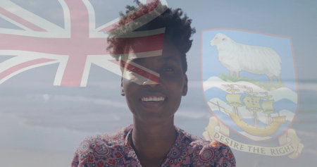 Smiling woman in red-white blouse on sandy beach, with Union Jack flag and coat-of-arms overlays. Portrait, leisure, vibrant, patriotism, empowerment, outdoor, celebrationの写真素材