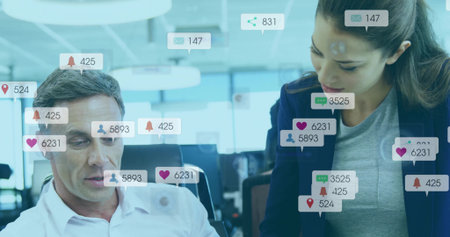 Collaborating coworkers in office attire reviewing laptop screen at desk with notification icons....