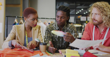 Three designers collaborating in fashion studio, with color palette, swatches and measuring tapes. Creative, collaboration, textile, craftsmanship, trendy, professional, inspiringの写真素材