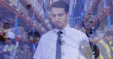 Viewing network overlay on tablet, man in white shirt, dark tie standing amid warehouse aisle. Logistics, supply chain, data analysis, industrial, teamwork, technology, collaborationの写真素材