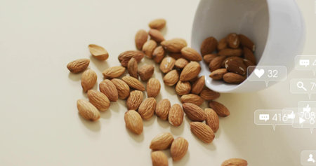 Spilling almonds from tipped white ceramic cup across kitchen tabletop, with social media icons. Snacks, health, branding, minimalist, lifestyle, natural, digitalの写真素材